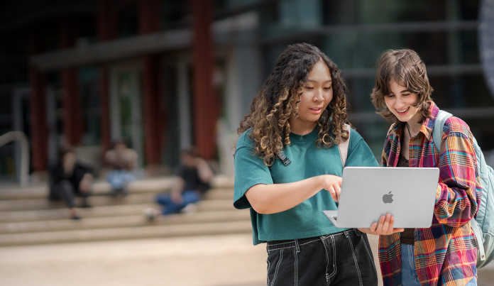 Deux personnes dehors sur le campus universitaire regardent l’écran d’un MacBook