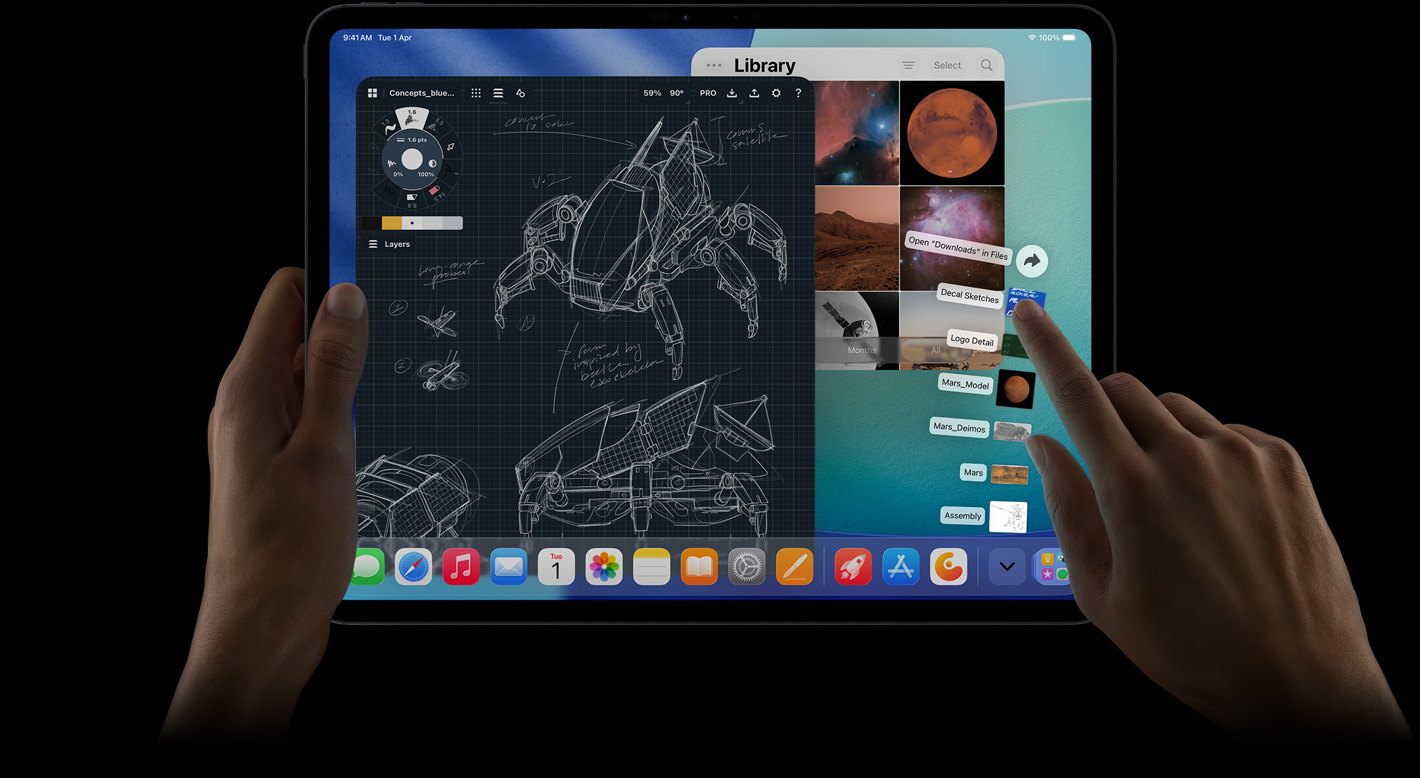 iPad Pro, front exterior, landscape orientation, right hand gesturing over Downloads folder files fanned out, display showing iPadOS 26 interface with multiple open apps including photo editing app with detailed robot blueprints and handwritten annotations and multiple design stages, and Photos Library