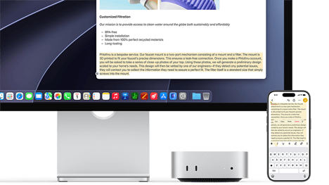 Mac mini front, tucked under Studio Display, an iPhone sits to the right of the device and the display, text selected with cut, copy, paste, and AutoFill commands above on iPhone matches highlighted text on display, showcasing Universal Clipboard