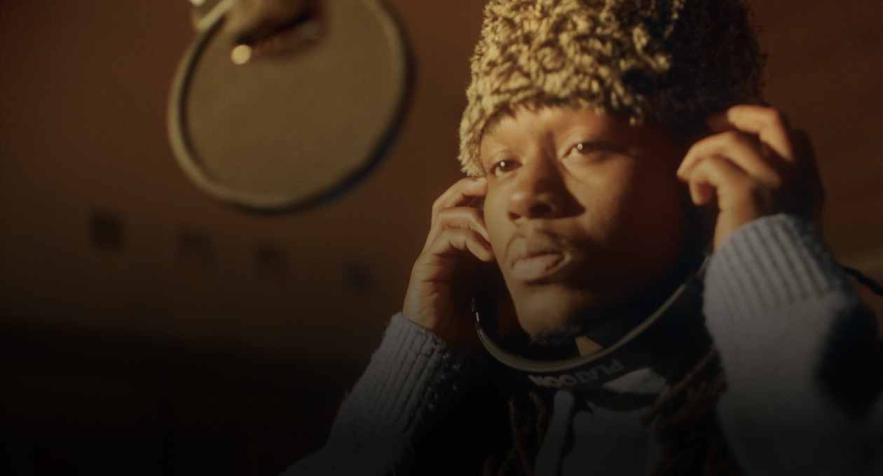 Ảnh Kiddo K trong studio âm nhạc đang đứng trước micrô ghi âm và nghe qua tai nghe