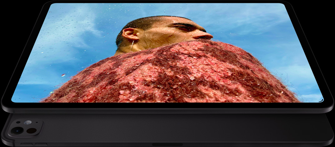 iPad Pro, front side exterior, landscape orientation, space black color, rounded corners, black display bezel, display showing a photo of a man in a red sweater under a blue sky, underneath, another iPad Pro, back exterior, landscape orientation, space black color, pro camera system, volume-up button, volume-down button