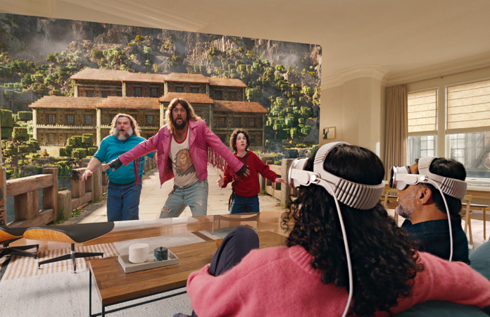 Two people both wearing Apple Vision Pro sit side by side on couch watching: A Minecraft Movie, displayed on screen stretching across room