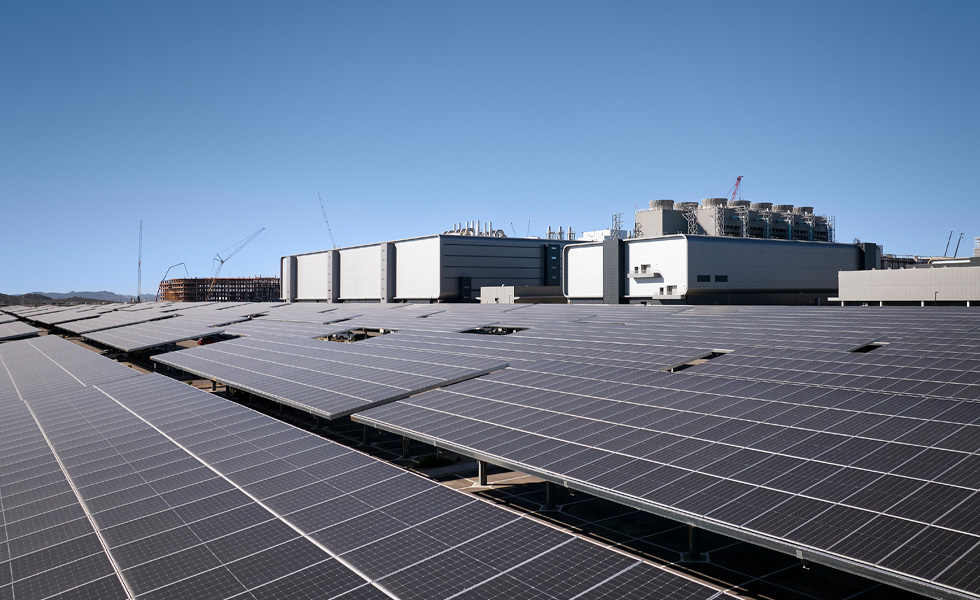 Rows of solar panels installed beside an industrial building under a clear blue sky