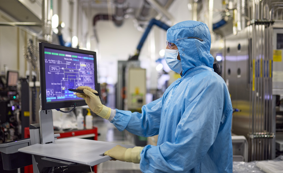 An employee in full-body work suit presses the touchscreen on a work station monitor